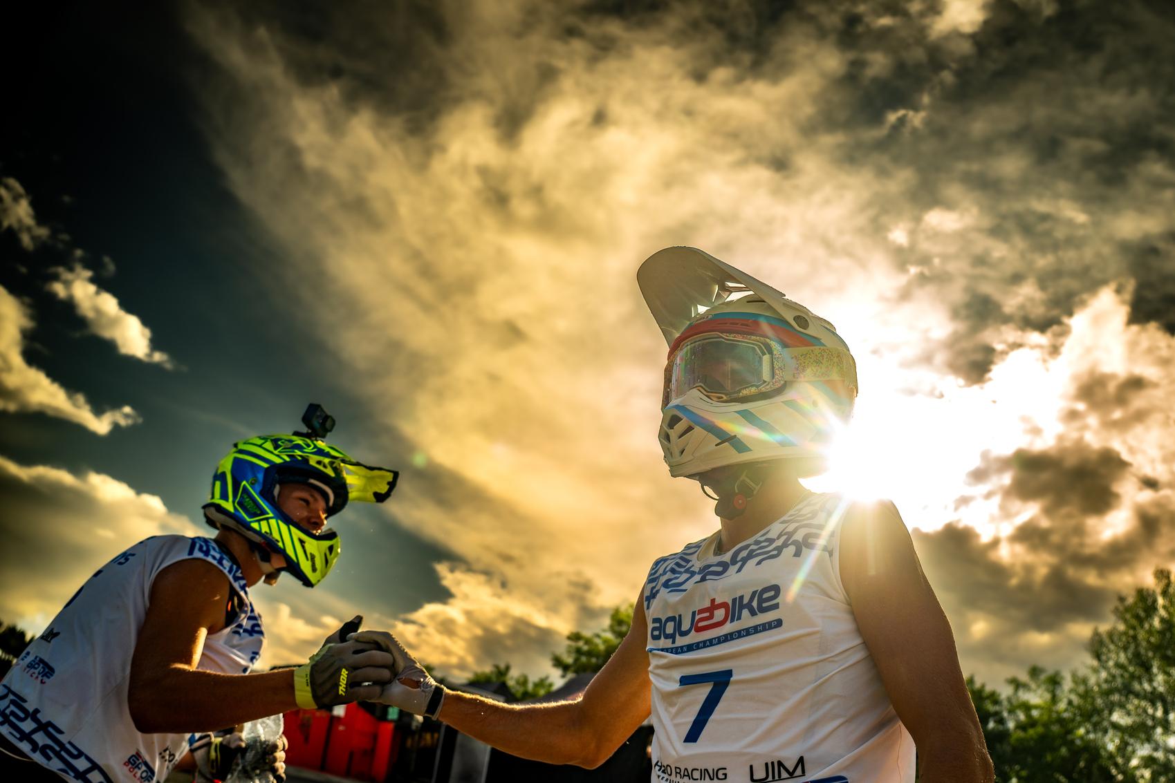 Atmosphere category gold: two aquabike riders in helmets shake hands against a dramatic cloudy sky in Gyor, Hungary