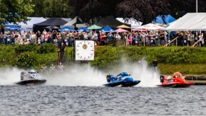Three Formula 2 catamarans blast from a dead-engine jetty start at Carr Mill Dam, St Helens, watched by a large crowd