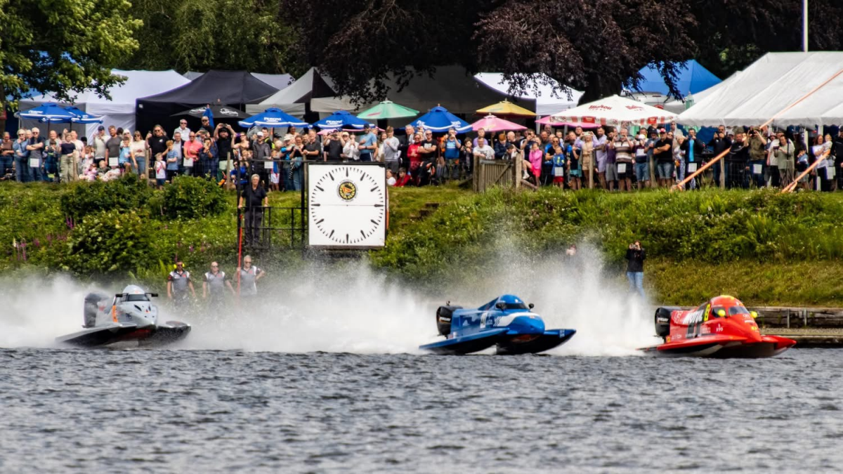 Three Formula 2 catamarans blast from a dead-engine jetty start at Carr Mill Dam, St Helens, watched by a large crowd