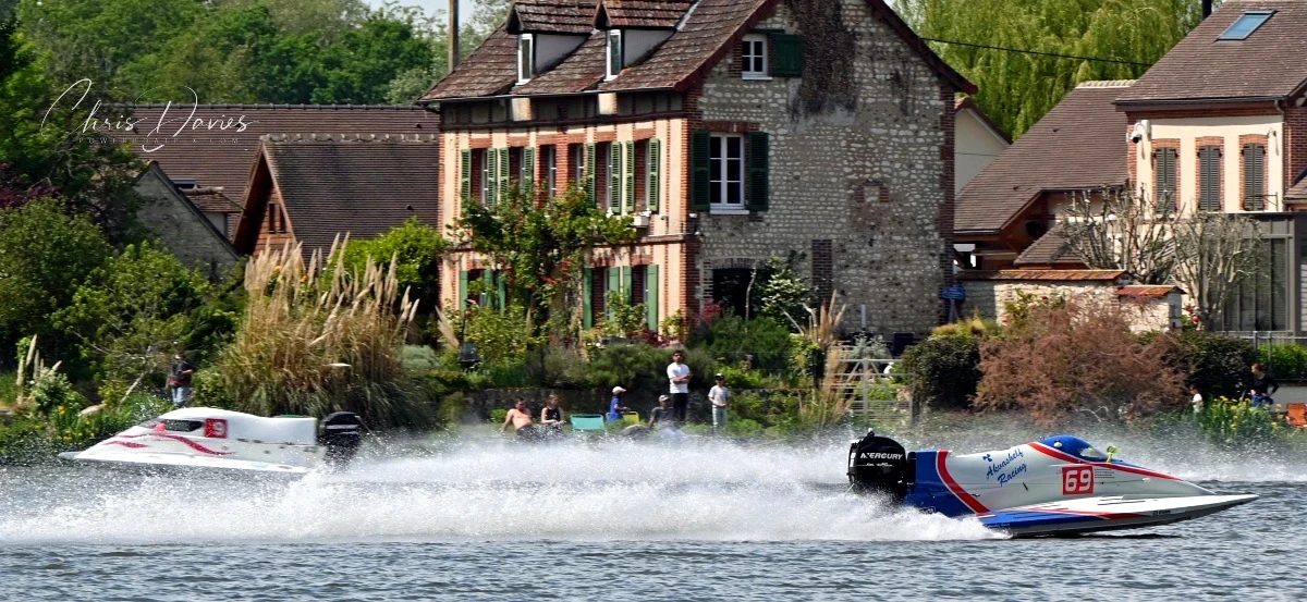 Boat 69 Akvashelf Racing on the River Seine at Poses during Race 2 of the 24 Heures Motonautiques de Normandie 2026, with riverside houses and spectators on the far bank