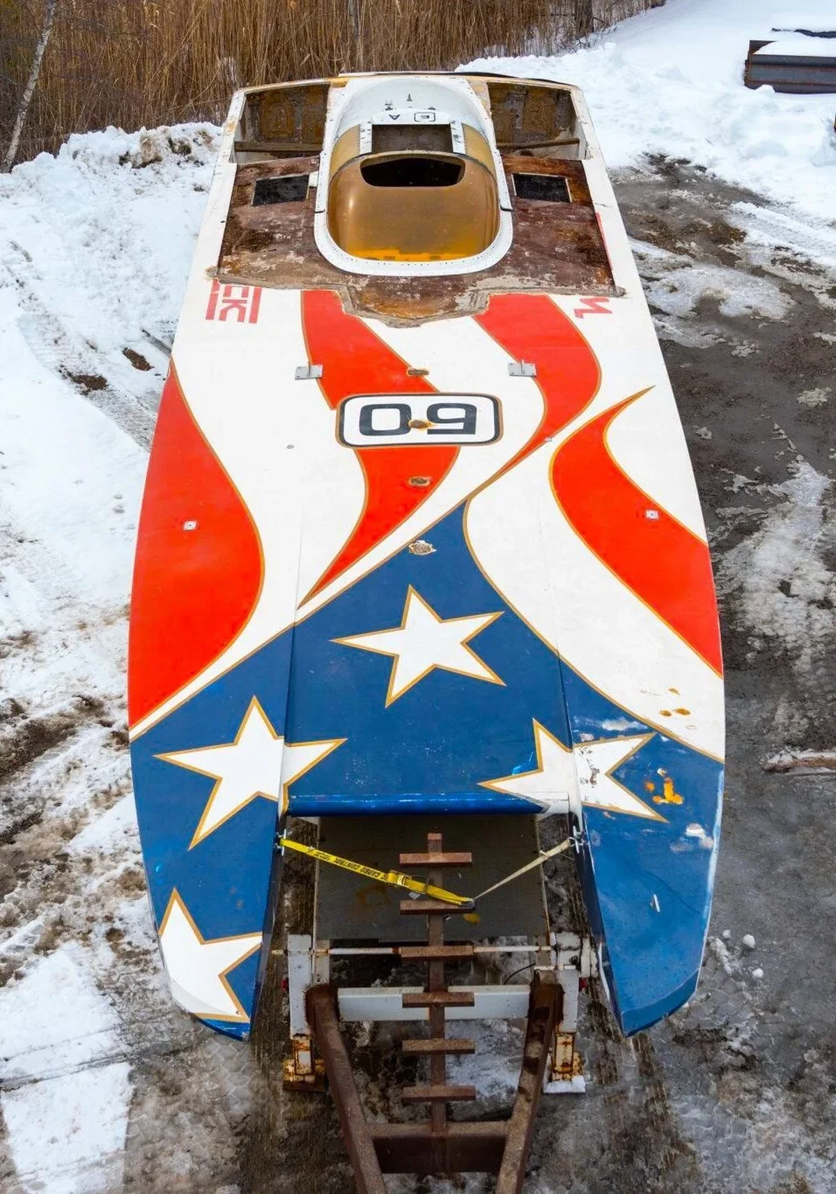 Don Johnson's Team USA catamaran today, aerial view showing faded stars-and-stripes livery and stripped hull on trailer in New Hampshire snow