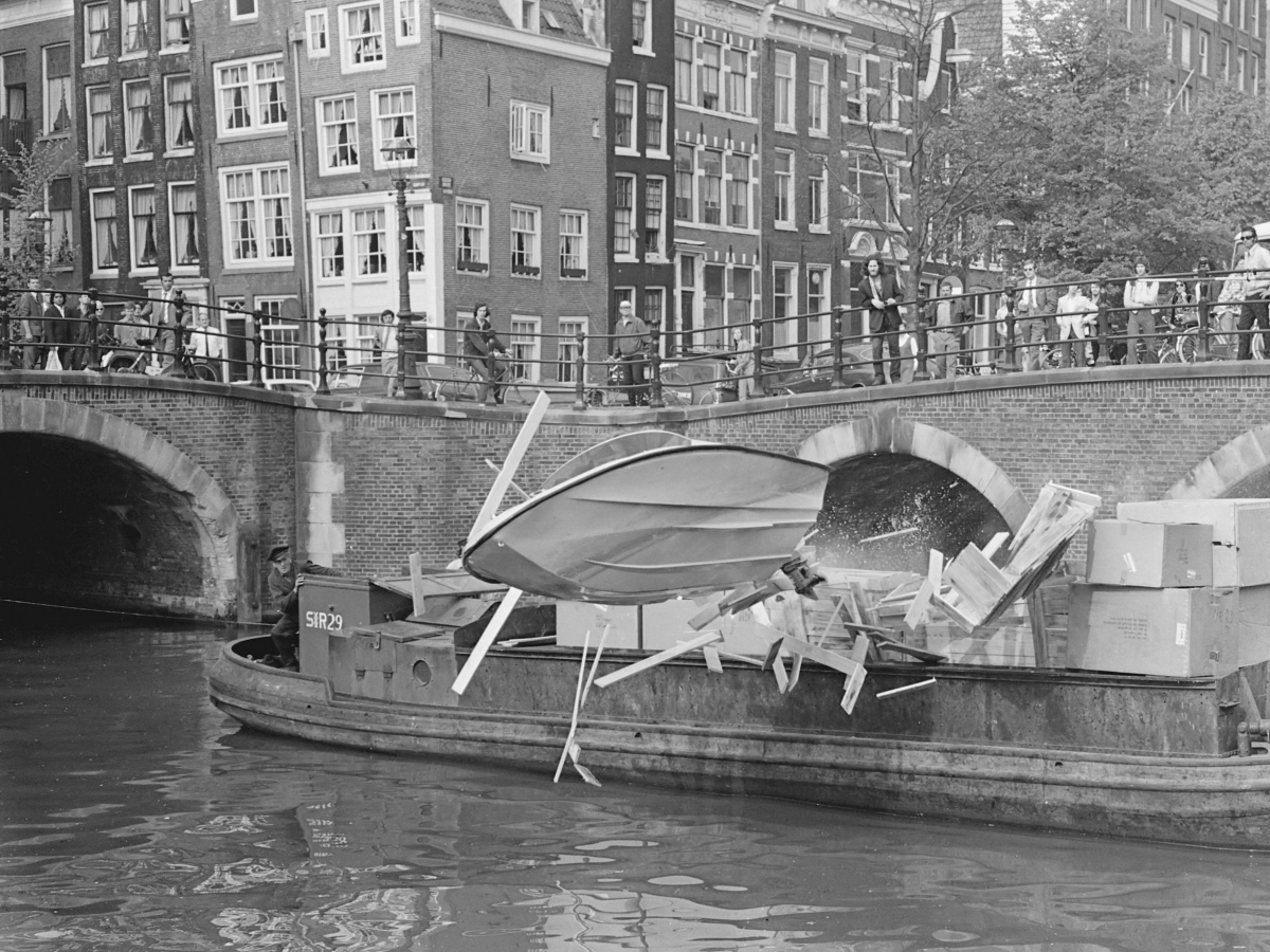 Wim Wagenaar drives a Shakespeare speedboat through crates on a barge during filming of Puppet on a Chain, Keizersgracht canal, Amsterdam, May 1970