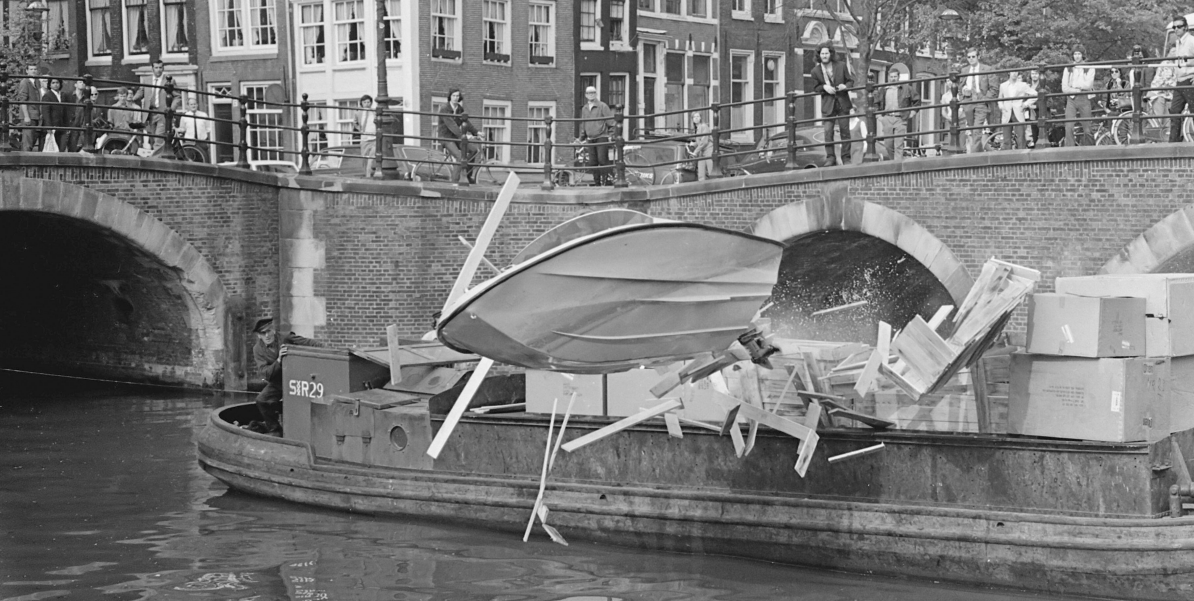 Wim Wagenaar drives a Shakespeare speedboat through crates on a barge during filming of Puppet on a Chain, Keizersgracht canal, Amsterdam, May 1970