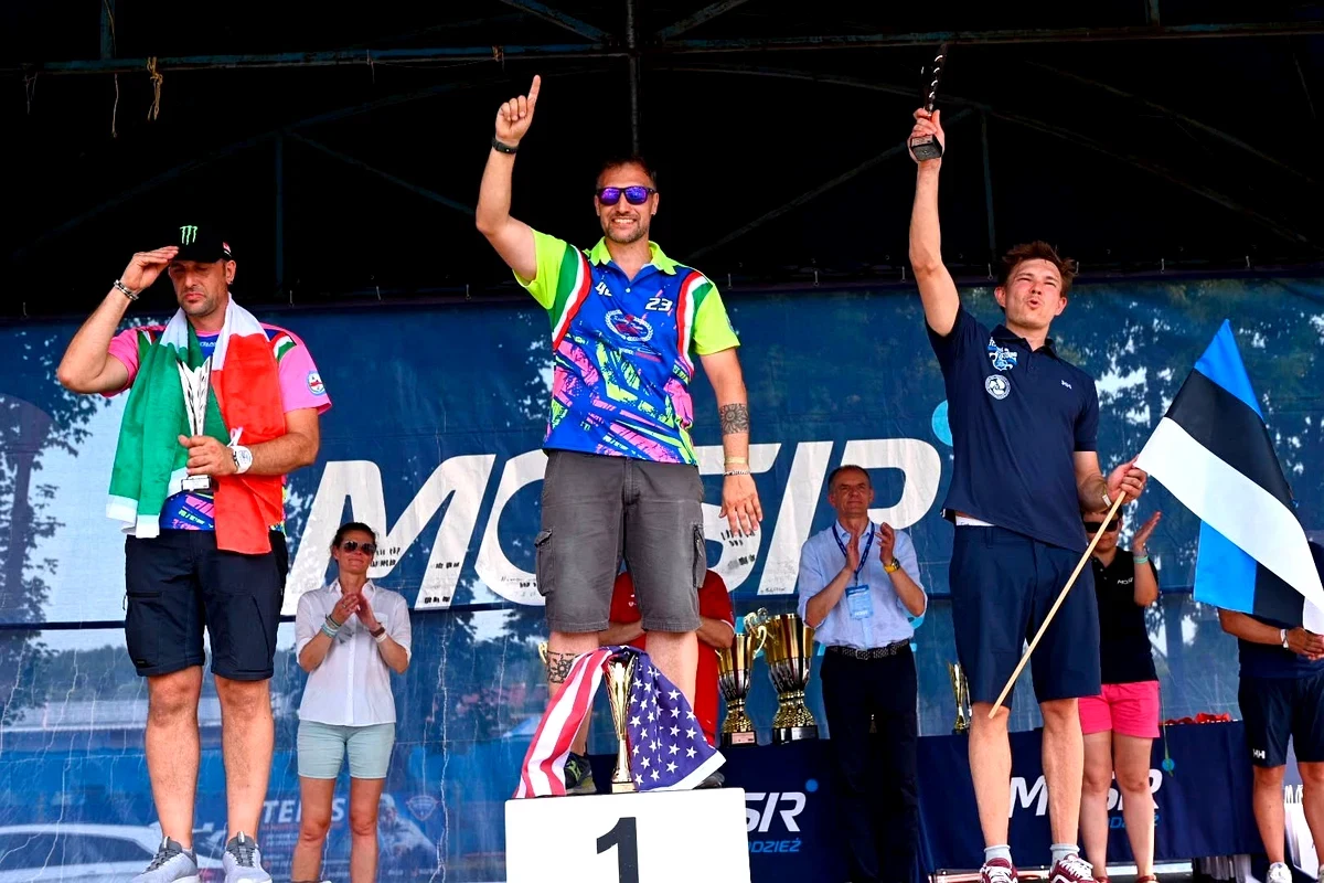 Driver on the top step of the podium at Chodziez celebrating an F.250 round win, with the US and Estonian flags on display