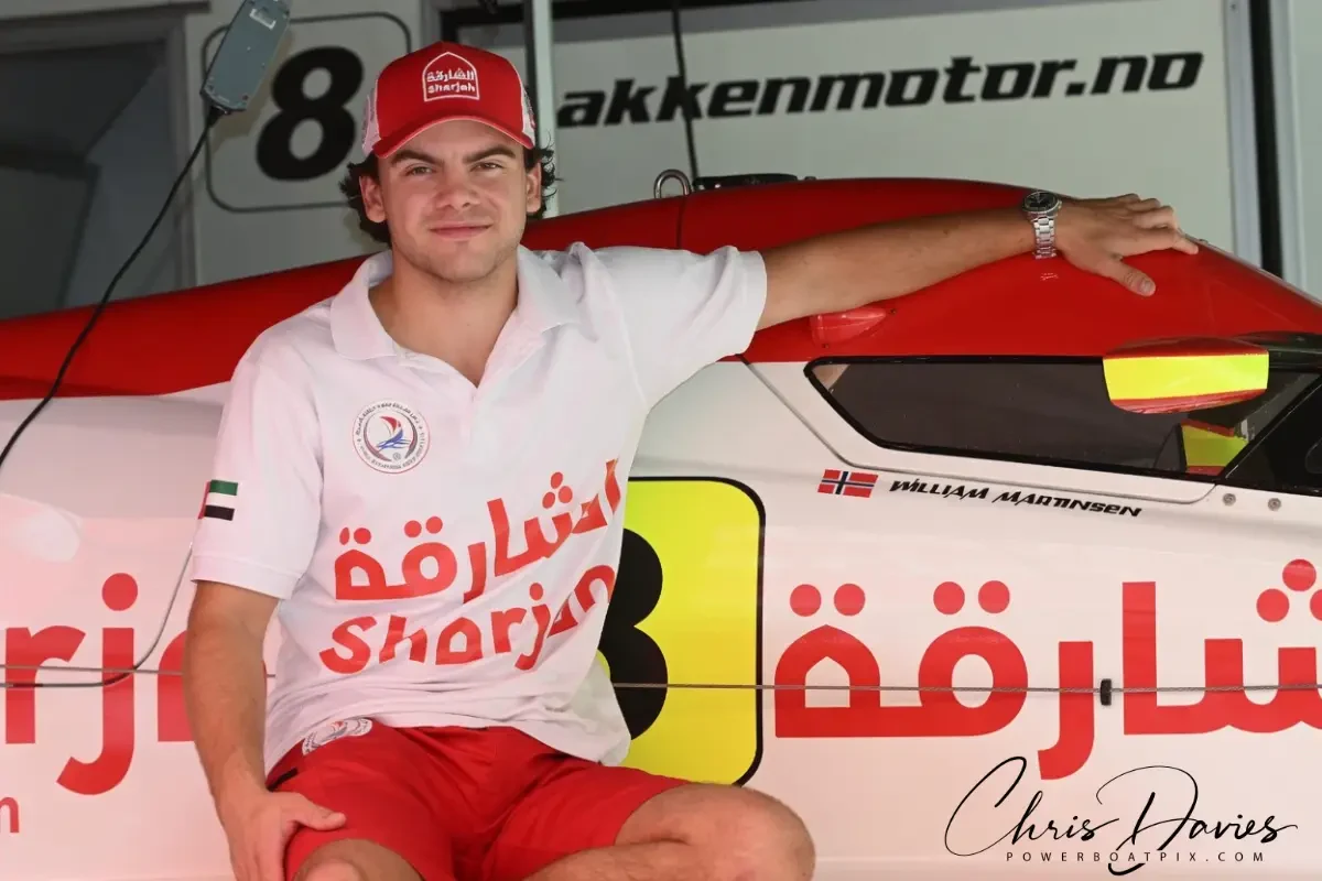 William Martinsen in Team Sharjah kit alongside the Formula 4 boat at Viverone, wearing a red Sharjah cap with his name and the Norwegian flag visible on the cockpit