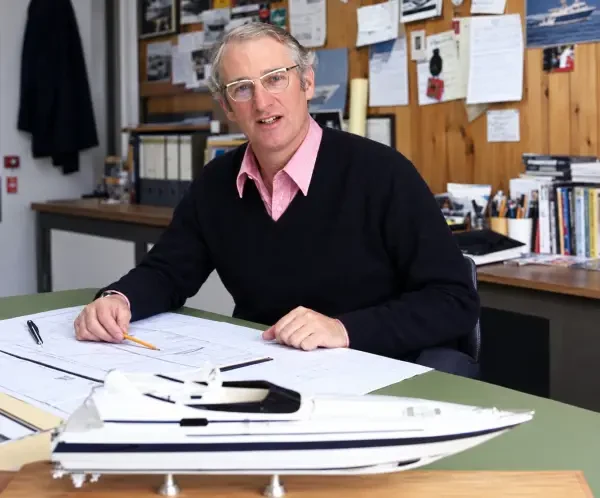 Don Shead at his drawing desk with a model motor yacht, surrounded by sketches and reference photos
