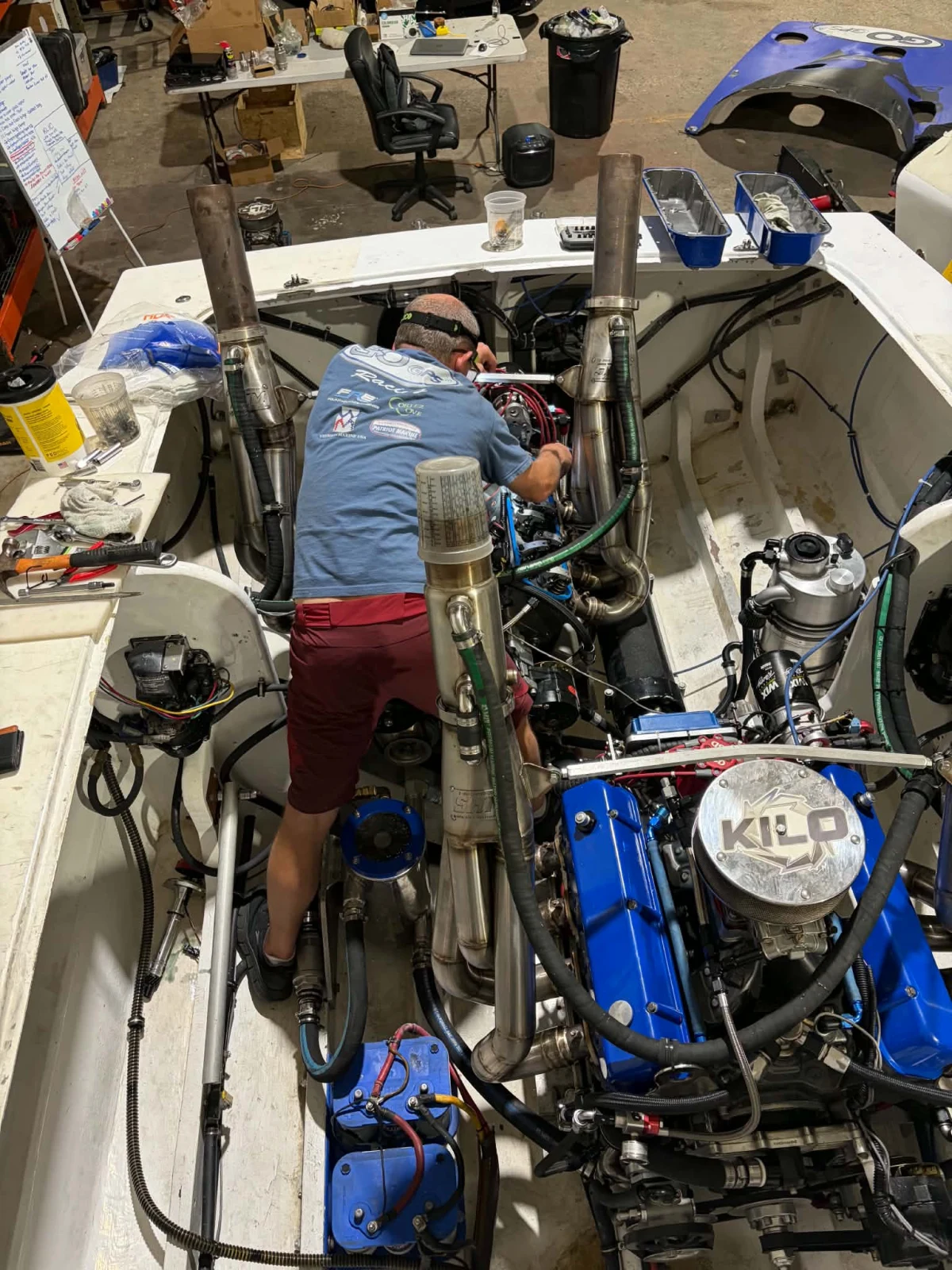 Team member in a Go GPS Racing shirt working in the engine bay of the Fountain, with blue engines, stainless exhaust stacks and a KILO blower cover