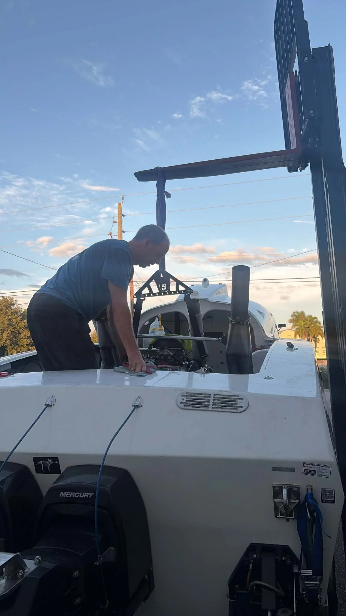 Team member leaning over the rear deck of the Fountain race boat beneath a lifting frame, with Mercury drives visible on the transom