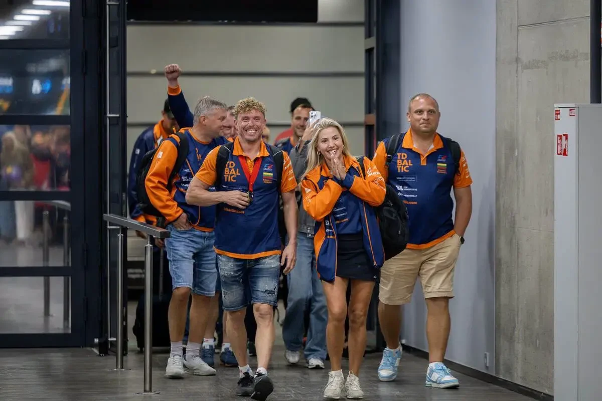 Edgaras Riabko and his team, in orange and blue team kit, walking through arrivals at Kaunas Airport after winning the 2026 UIM F2 World Championship