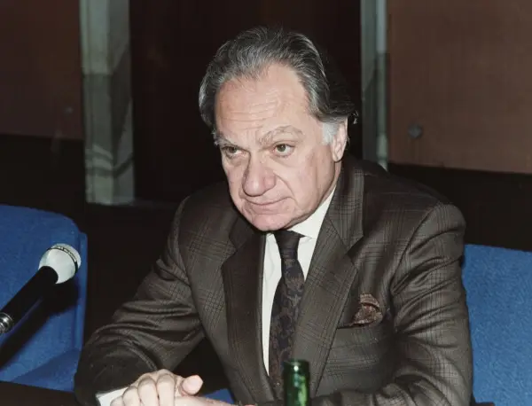Arrigo Gattai in a checked suit seated at a table with a microphone