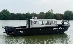 Cox Marine test and development vessel Miranda, a black Tideman RBC1200 HDPE workboat with white wheelhouse and twin Cox Marine V8 diesel outboards, under way on a river
