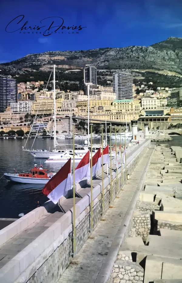Monegasque flags at half-mast along the Monaco harbour wall, with the town and Mont Agel behind, October 1990