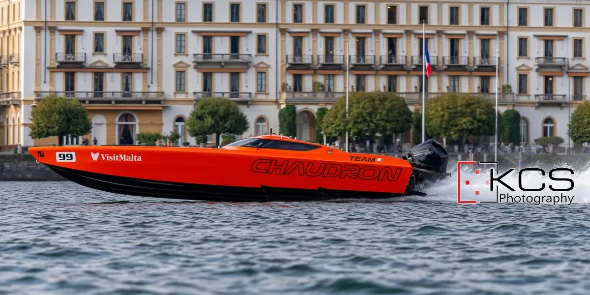 The orange Team Chaudron monohull, number 99, passing Villa d'Este at the 2026 Centomiglia del Lario